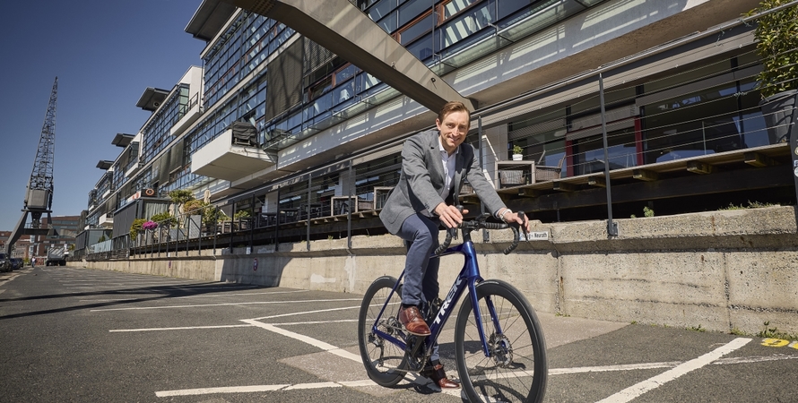 Man cycling along a quay beneath a container cranes, with port and terminal infrastructure visible in the background.